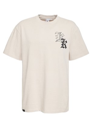 Beżowy bawełniany T-shirt z krótkim rękawem, z czarnym stylizowanym nadrukiem litery "K" na lewej piersi oraz małą metką marki przy dolnym szwie.