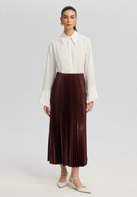 Camicia bianca con colletto e maniche lunghe abbinata a una gonna midi plissettata borgogna. La gonna presenta una texture liscia e una leggera lucentezza.