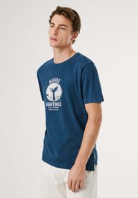 Camiseta de algodón azul oscuro, de cuello redondo, con mangas cortas, que presenta una impresión gráfica blanca de una cola de ballena y el texto "Avistamientos Marinos."
