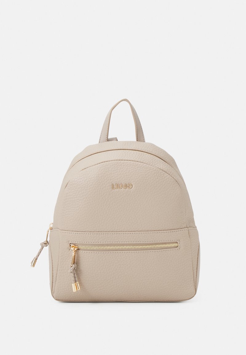 Petit sac à dos beige texturé avec fermeture éclair dorée et logo de marque, doté d'une poignée supérieure et d'une poche avant zippée.