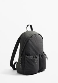 Sac à dos gris foncé de forme arrondie, en tissu doux, avec deux poches avant à cordon de serrage et des bretelles rembourrées.
