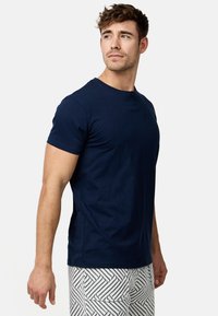 T-shirt bleu marine à manches courtes avec un col rond et un détail de bouton unique, fabriqué à partir d'un tissu doux et texturé. Associé à un short à motifs.