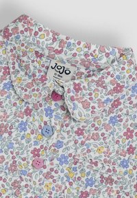 Baumwollbluse mit Blumendesign auf weißem Grund, mit bunt gemusterten Blumen, einem Kragen und rosa, blauen und gelben Knöpfen.