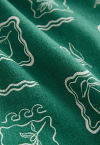 Green fabric with white abstract patterns, including wavy lines and leaf shapes. The texture appears smooth and slightly woven.