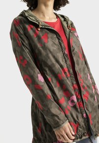 Veste légère à capuche en vert olive avec des motifs floraux rouges et roses, équipée d'une fermeture éclair à l'avant et de poignets élastiques pour un ajustement parfait.