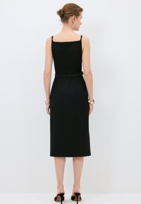 Schwarzes Midikleid mit quadratischem Ausschnitt, dünnen Trägern, tailliertem Bund und figurbetonter Silhouette. Der Stoff hat eine glatte Textur und klare Linien.