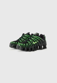 Black athletic shoes featuring green accents and a mesh upper, with a ribbed design and a distinctive cushioned sole.