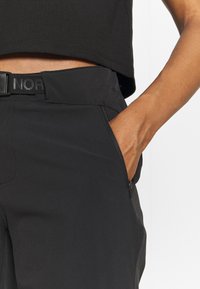 Svarta tekniska byxor har en figurnära design, blixtlåsfickor på sidan och en texturerad midja med präglad logotyp. Slät, lättviktsmaterial.