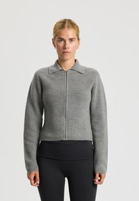 Grijze geribbelde ritstrui met een kraag en lange mouwen, gemaakt van een gestructureerd breimateriaal. Korte pasvorm op de taille.