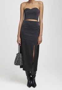 Ensemble noir en deux pièces comprenant un top court sans bretelles et une jupe taille haute avec une fente avant. Associé à un sac texturé noir et blanc.