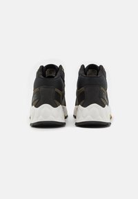 Zapatillas altas negras y verdes oliva con tejido texturizado y detalles de cuero. Suela intermedia gruesa y blanca, y suela de goma con un patrón de relieve prominente.