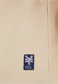 Bežna tkanina s dijagonalnom teksturom, s plavim mrljama na kojima se nalazi bijeli logo i tekst "ZOO YORK" u donjem desnom kutu.