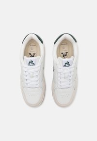 Scarpe da ginnastica bianche con finitura in pelle liscia, dettagli verdi sul tallone e lacci bianchi. Presentano un'area della punta perforata e un logo sulla linguetta.