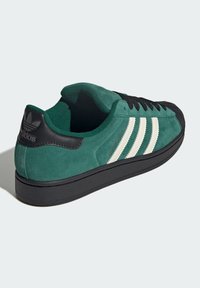 Groene suède sneaker met zwarte accenten en rubberen zool. Heeft drie witte strepen en een logo op de hiel. Ronde neus en vetersluiting ontwerp.