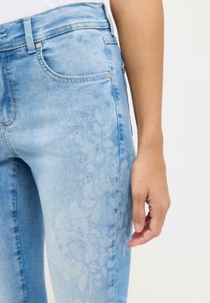 Hellblaue Jeans mit einem dezenten Blumenmuster und Verzierungen aus kleinen Strasssteinen auf der Vorderseite. Standard-Denim-Taschen sind sichtbar.
