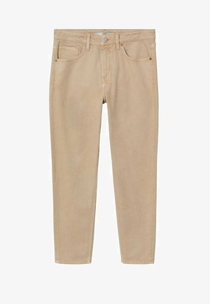 Mann trägt einen beigen kurzärmeligen Pullover, hellbraune gerade Hosen und weiße Sneakers mit Gummisohlen, steht vor einem schlichten Hintergrund.