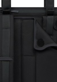 Gros plan d'un sac en tissu noir avec des sangles, une fermeture éclair et un rabat en Velcro, mettant en évidence la texture et les coutures.