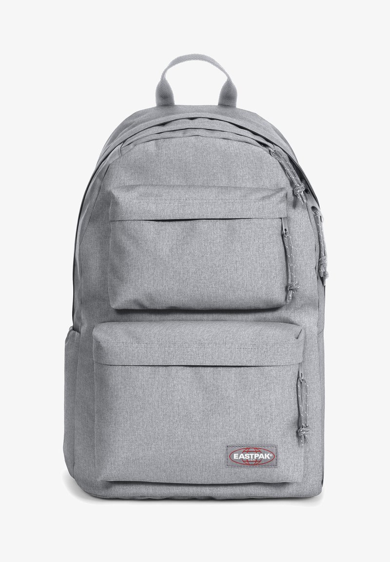 Mochila de tela gris con dos bolsillos frontales con cremallera, respaldo acolchado y detalles cosidos. Presenta el logo de Eastpak en la parte frontal inferior.