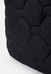 Saco acolchoado preto com padrão hexagonal e textura suave. Apresenta um discreto logótipo em relevo "BORG" de um lado.