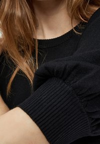 Černý pletený svetr s žebrovanými manžetami a kulatým výstřihem, který se vyznačuje jemnou texturou a přiléhavým střihem.