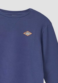 Blaues Langarm-Sweatshirt mit geripptem Muster, das ein orangefarbenes, rautenförmiges Sticklogo auf der Brust und einen klassischen Rundhalsausschnitt aufweist.