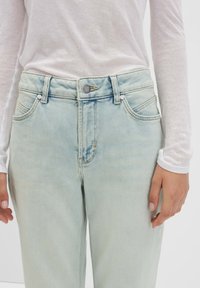 Hellblaue Jeans aus Denim mit hoher Taille, einem Fünf-Taschen-Design und einem silbernen Knopfverschluss. Sie verfügen über dezente Verwaschungen und Stickdetails.