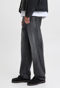 Platu piegriezuma, izbalējušas melnas džinsa auduma bikses. Tās ir ar taisnu siluetu, redzamām šuvēm un nodilušu tekstūru. Kombinētas ar melniem apaviem.