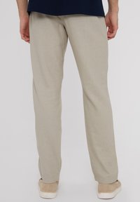 Beige Leinenhosen mit geradem Schnitt, die ein schlichtes Design und eine glatte Textur aufweisen, getragen mit hellen, lässigen Schuhen.