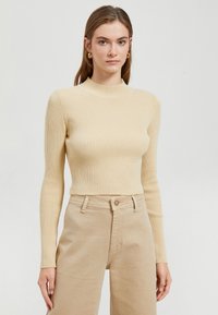 Ribbed beżowy skrócony sweter z długimi rękawami i wysokim dekoltem, w połączeniu z beżowymi spodniami o wysokim stanie. Gładka textura na całej powierzchni.