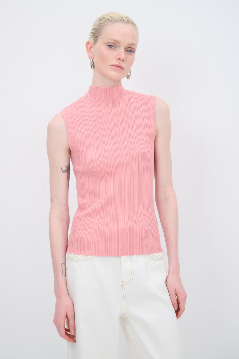 Mouwloze, hoge-nektop van ribstof in zachtroze stof; de aansluitende pasvorm benadrukt de silhouet; gestyled met witte wijde broek en minimale accessoires.