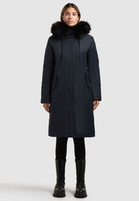 Parka blu navy con colletto in pelliccia sintetica, dotata di zip frontale, tasche laterali e design fino al ginocchio. Tessuto testurizzato e vestibilità slanciata.