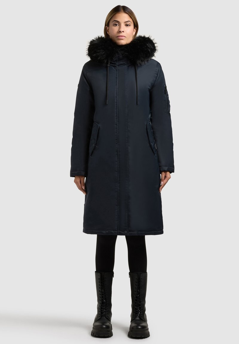 Parka blu navy con colletto in pelliccia sintetica, dotata di zip frontale, tasche laterali e design fino al ginocchio. Tessuto testurizzato e vestibilità slanciata.