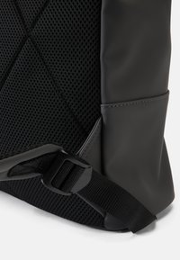 Svart ryggsäckshörn med vadderad mesh baksida, justerbar rem med plastspänne och släta syntetiska sidomaterial.