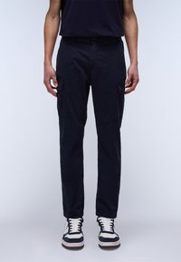 Navy cargo pants made of cotton. Features two side pockets, regular fit, and a slightly tapered leg. Worn with high-top sneakers.