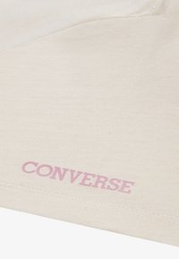 Beige bomullstyg med en texturerad yta, med en framträdande rosa "CONVERSE"-logotyp. Enkelt design utan ytterligare mönster eller detaljer.