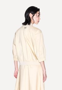 Bomber jacket beige chiaro con vestibilità rilassata, polsini ed orlo elasticizzati. Realizzato in materiale morbido, presenta un dettaglio del logo sulla schiena.