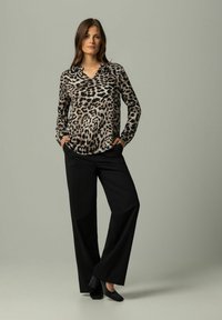 Bluzka z długim rękawem w wzór lamparta z dekoltem w serek, zestawiona z czarnymi spodniami w szerokim kroju i czarnymi butami, na neutralnym tle.