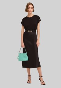 Vestido negro con mangas cortas y un cinturón. La modelo lleva un bolso verde menta y sandalias negras de tiras. Diseño simple y elegante.