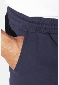 Marineblaue Jogginghose mit elastischem Bund, ausgestattet mit einer Seitentasche und einer glatten, weichen Textur, in der Aufnahme auf Hüfthöhe.