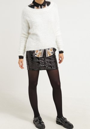 Suéter blanco esponjoso, falda negra de lentejuelas, medias negras y zapatos negros texturizados con hebillas. Camisa con patrón debajo del suéter.