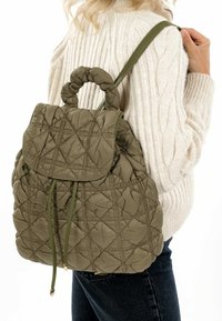 Sac à dos olive matelassé avec une poignée supérieure et une bandoulière réglable. Caractéristiques d'une fermeture rabat et d'une broderie en motif losange.