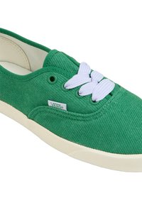 Green canvas sneaker with white laces, rounded shape, and cream-colored sole. Features a textured surface and a logo tag on the side.