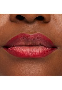 Gros plan sur des lèvres à la peau foncée avec un rouge à lèvres rouge brillant, montrant la texture naturelle et un léger éclat.