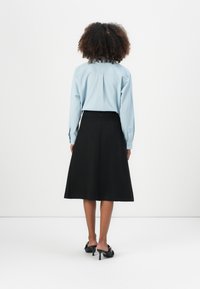 Lichtblauwe blouse met lange mouwen en achterplooien, gecombineerd met een zwarte A-lijn rok met een textuurpatroon, en zwarte pumps.