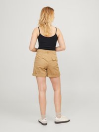 Pantaloni scurți din bumbac bej, cu margini răsucite, buzunar lateral și croială lejeră, asortați cu un top negru fără mâneci și adidași albi casual.