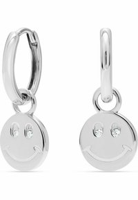 Orecchini a cerchio in argento con pendente a faccina sorridente, decorati con due piccole gemme per gli occhi, texture liscia e finitura lucida.