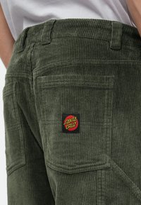 Πράσινα παντελόνια καμπάνα από κοτλέ με λογότυπο "Santa Cruz" σε ράμμα, ορατά ράμματα και πολλαπλές τσέπες στο πίσω μέρος.