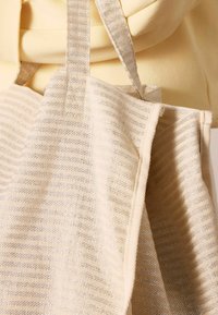 Beige tas met textuurstrepen en metalen accenten. Heeft stevig materiaal en platte hengsels voor gemakkelijk dragen.