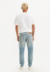 Camiseta de algodón blanca y jeans de un azul claro con un ligero efecto de desgaste. Los jeans tienen un parche de cuero marrón y bolsillos traseros.
