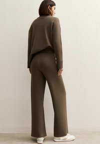Ensemble en tricot brun comprenant un pull et un pantalon large. Le tissu a une texture douce. La tenue est décontractée et est associée à des baskets blanches.
